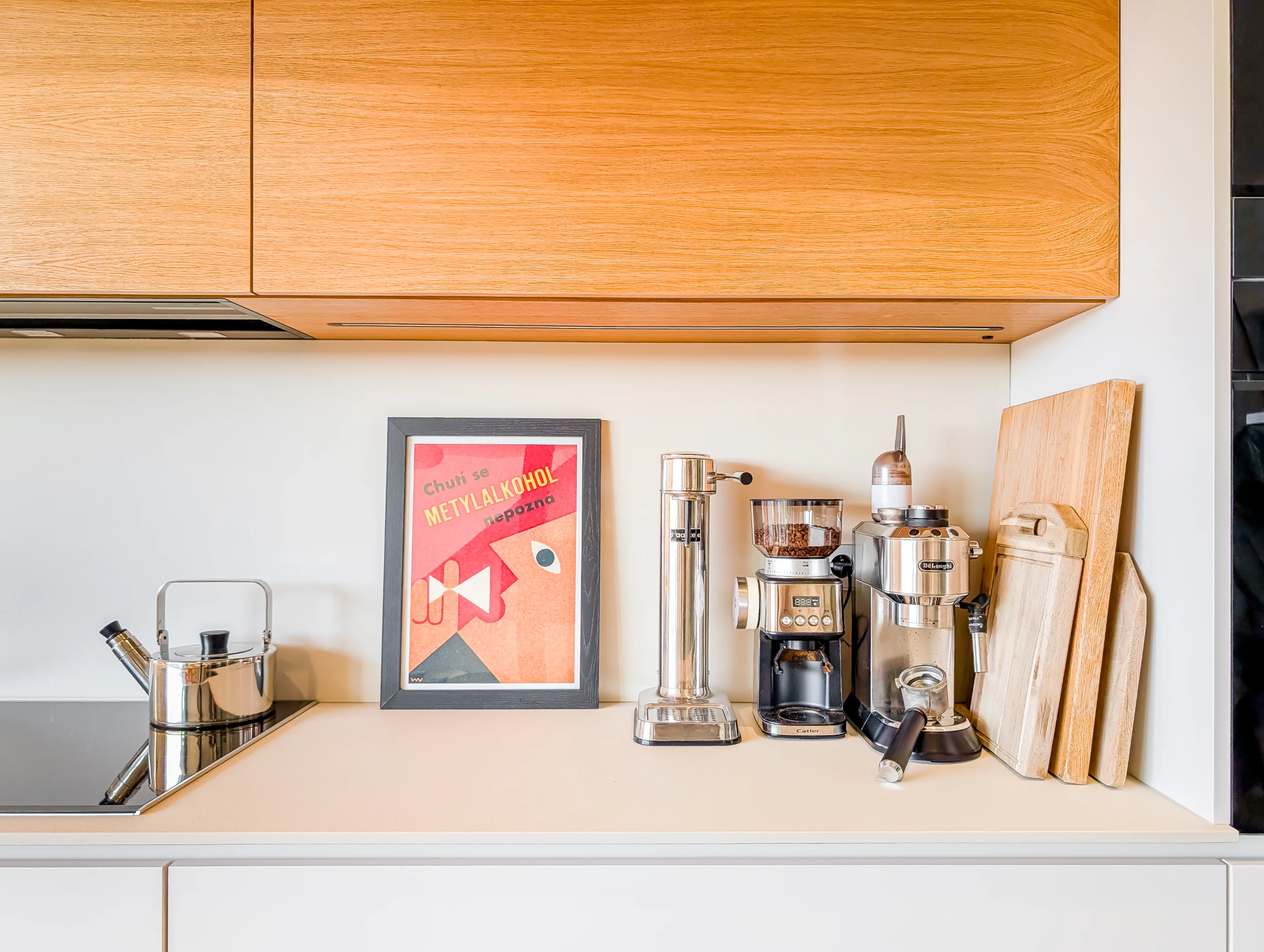 Světlé kuchyňské lince dominuje kávovar s dřevěnými skříňkami.